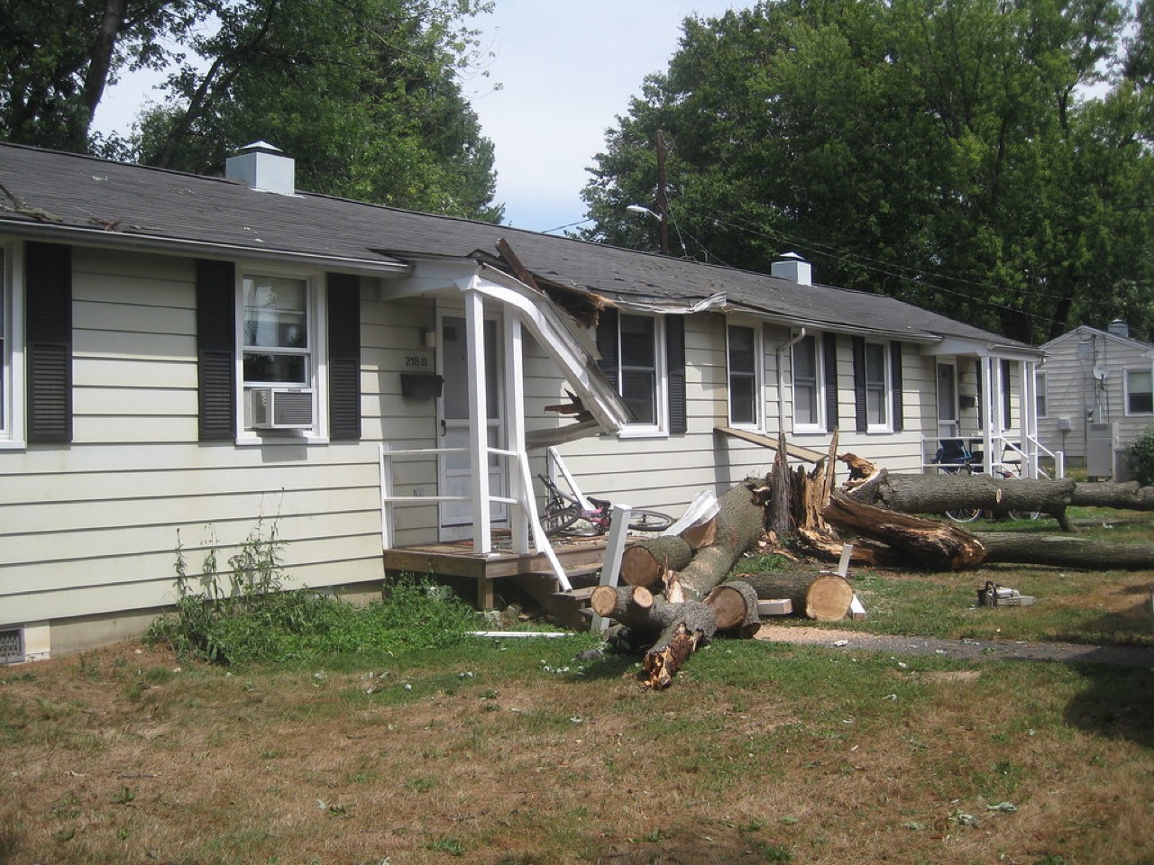 Storm-downed tree fallen against a Belton home, damaging the roofline with the trunk cut into sections across the front yard during emergency tree removal cleanup